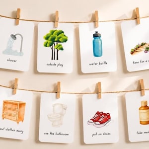 Op de afbeelding: Een set van acht geïllustreerde kaarten die met houten wasknijpers aan een touwtje zijn geklemd. Elke kaart toont een dagelijkse activiteit, waaronder een douche, een boom, een waterfles, een wandeling, kleding opruimen, naar de badkamer gaan, schoenen aantrekken en medicijnen innemen.