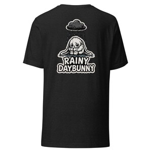 May include: Dark grey t-shirt with a black and white graphic of a sad bunny under a rain cloud. The text "RAINY DAYBUNNY" is below the bunny. The t-shirt has a crew neck design.