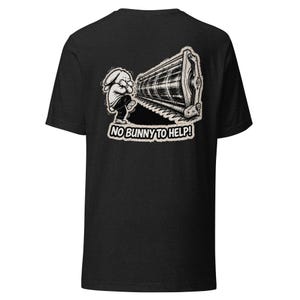 Może przedstawiać: Czarny t-shirt z zabawną grafiką. Projekt przedstawia kreskówkowego królika i dużą maszynę z napisem "NO BUNNY TO HELP!". Koszulka wykonana jest z miękkiego materiału.