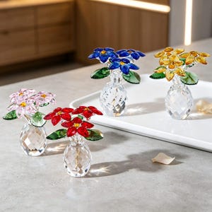 May include: Four small crystal flower figurines in clear faceted vases. Each features colorful petals in pink, red, blue, or yellow with green crystal leaves and a central yellow accent. The clear vases have a diamond-cut pattern on the surface.