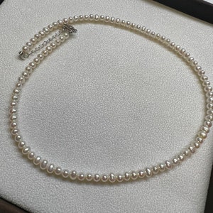 Può includere: Una collana di perle bianche con una chiusura argentata. La collana è composta da piccole perle rotonde e misura circa 40 cm di lunghezza.