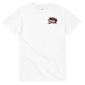 Może przedstawiać: Biały t-shirt z krótkim rękawem z małą grafiką w lewej górnej części klatki piersiowej. Wzór zawiera napis JDM pogrubioną czarną czcionką, czerwone słońce, czarną sylwetkę pagody oraz drobne akcenty w postaci różowych kwiatów wiśni.