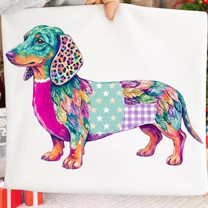 Puede incluir: Un cuadrado de tela blanca con una colorida ilustración de un perro salchicha. El perro tiene la cabeza de color verde azulado con orejas de leopardo, el pecho rosa brillante y el cuerpo cubierto de plumas multicolores, estrellas y cuadros.