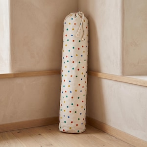 May include: A tall, cylindrical fabric storage bag featuring an off-white base colour with a repeating pattern of small, multicoloured polka dots in shades of red, blue, green, and yellow, finished with a drawstring closure at the top.