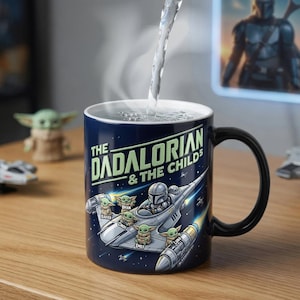 以下が含まれることがあります： 黒い持ち手が付いた、紺色のセラミックマグカップ。「The Dadalorian & The Childs」の文字と、宇宙船のグラフィック、ベビーヨーダのキャラクターが描かれています。マグカップに水が注がれています。