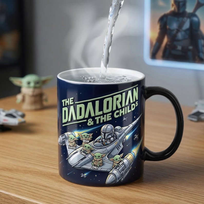 以下が含まれることがあります： 黒い持ち手が付いた、紺色のセラミックマグカップ。「The Dadalorian & The Childs」の文字と、宇宙船のグラフィック、ベビーヨーダのキャラクターが描かれています。マグカップに水が注がれています。
