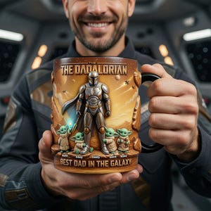 May include: A ceramic mug with a design inspired by The Mandalorian. The mug has a brown and gold colour scheme with the text "THE DADALORIAN" and "BEST DAD IN THE GALAXY". The design includes the Mandalorian, Grogu, and the names of the children.