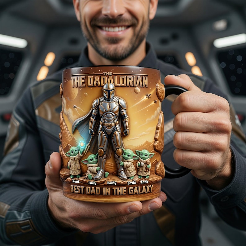 May include: A ceramic mug with a design inspired by The Mandalorian. The mug has a brown and gold colour scheme with the text "THE DADALORIAN" and "BEST DAD IN THE GALAXY". The design includes the Mandalorian, Grogu, and the names of the children.