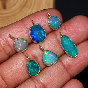 May include: A collection of opal pendants with gold-colored settings. The opals display a range of colors, including blues, greens, and hints of other hues. The pendants vary in shape, including oval, teardrop, and irregular forms.