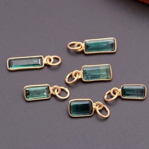 K&ouml;nnte beinhalten: Sechs rechteckige Anh&auml;nger mit tiefgr&uuml;nen, durchscheinenden Steinen in goldfarbenen Metallfassungen. Jeder Anh&auml;nger verf&uuml;gt &uuml;ber einen kleinen, runden Biegering an einem Ende, der eine einfache Befestigung an Schmuckketten oder anderen Teilen erm&ouml;glicht.
