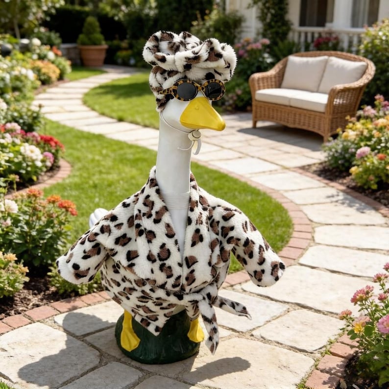 May include: A white goose statue wearing a plush leopard print bathrobe with a matching head wrap and leopard print sunglasses. The goose has a bright yellow beak and is positioned on a dark green base, showcasing a detailed animal print outfit.