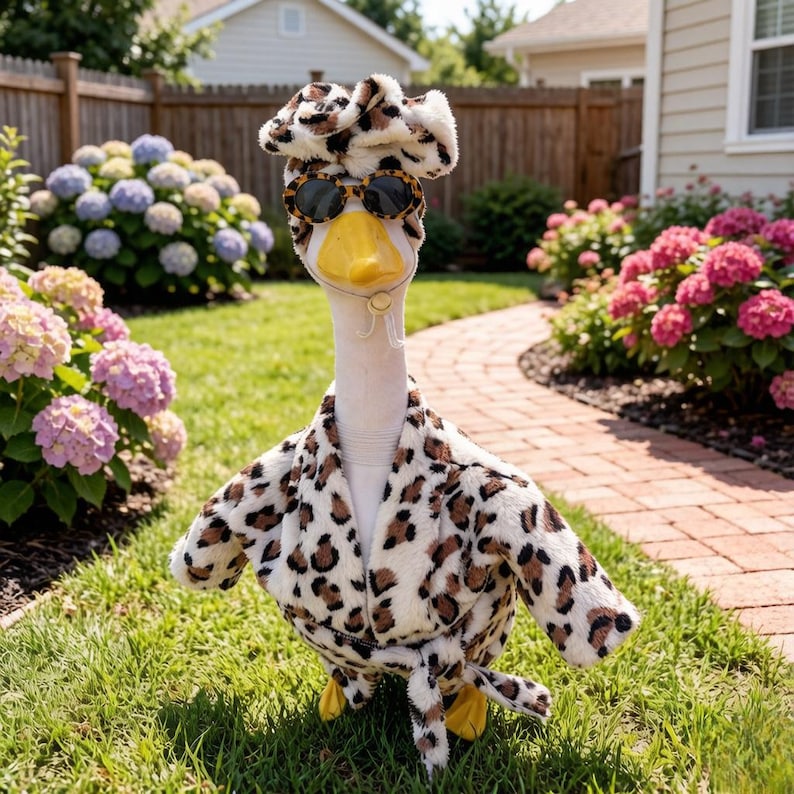 May include: A white goose figurine wearing a plush leopard print bathrobe and a matching leopard print headband. The goose is accessorized with round leopard print sunglasses that have dark lenses and a small white chin strap.