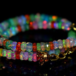 Puede incluir: Un collar o pulsera compuesto por pequeñas cuentas de ópalo facetadas y multicolores en tonos azul, verde, naranja y blanco translúcido. La pieza está rematada con un cierre de metal dorado con forma de pequeña flor o campana ornamentada.