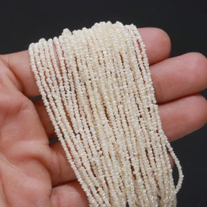 May include: A collection of multiple strands of small, off-white, irregular seed pearls. The pearls are strung together in long, thin lines, showcasing a textured, bumpy surface and a soft, natural luster characteristic of genuine freshwater pearls.