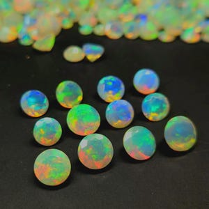May include: A collection of round, faceted opal gemstones displaying a translucent white base with vibrant flashes of green, blue, orange, and yellow iridescence. The stones are arranged in a cluster on a dark surface, showcasing their play-of-color.