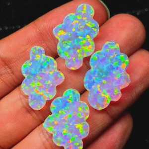 Könnte beinhalten: Vier wolkenförmige Cabochons aus synthetischem Opal. Jedes Stück hat eine durchscheinende weiße Basis mit einem lebendigen Farbspiel, das schillernde Blitze in Neongrün, hellem Gelb und elektrischem Blau auf der gesamten Oberfläche zeigt.