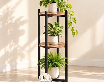 Puede incluir: Un soporte para plantas de tres niveles con marco de metal negro y estantes circulares con vetas de madera. Cada estante sostiene una planta en maceta, incluyendo una enredadera, una planta de hojas verdes y un helecho. Logo LuckyCraftsHub visible.