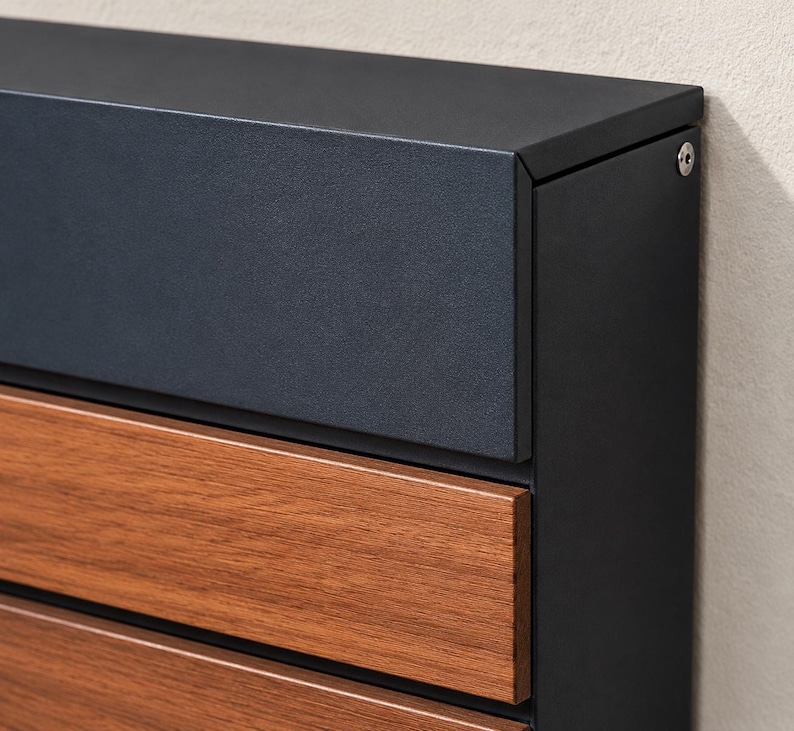 Puede incluir: Un buz&oacute;n de pared con marco de metal negro mate y tapa superior, con paneles horizontales de acabado en tono madera c&aacute;lida. La estructura incluye una cabeza de tornillo circular de color plateado visible en la esquina superior derecha.