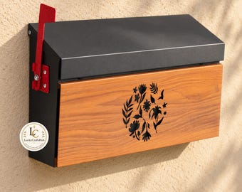 Puede incluir: Un buzón de pared con marco de metal negro mate, panel frontal de madera con diseño de silueta floral negra y una bandera de metal rojo brillante en el lado izquierdo. Se observa un pequeño logotipo circular con el texto LuckyCraftsHub.