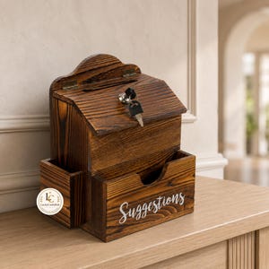 May include: A dark brown stained wooden suggestion box with a slanted top, a metal lock with a key, and a side compartment. The front of the box features the word "Suggestions" in white script lettering and a small circular logo with the text "LuckyCraftsHub".