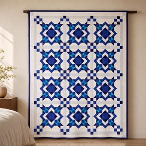 Op de afbeelding: Een rechthoekige quilt met een herhalend geometrisch sterpatroon in tinten marineblauw, koningsblauw en lichtblauw op een witte achtergrond. Het ontwerp bevat een donkerblauwe rand en een raster van onderling verbonden stermotieven.