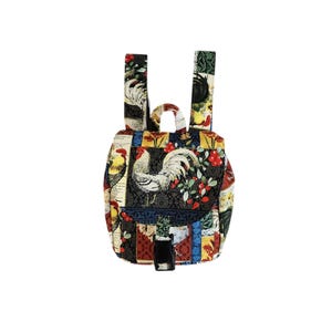 Puede incluir: Una pequeña mochila multicolor con estampado de gallo y flores. La mochila tiene un cierre de hebilla negra y correas ajustables.