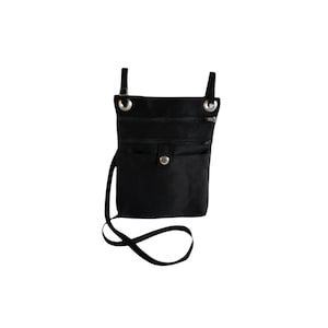 May include: Black crossbody bag with multiple zippered compartments and a snap closure. The bag has a long, adjustable strap and metal hardware. The bag is designed to be worn over the shoulder or across the body.