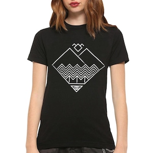 Può includere: Una t-shirt nera a maniche corte con una stampa grafica bianca sul petto. Il design consiste in una forma a diamante contenente una cima di montagna, una serie di linee orizzontali a zigzag e un piccolo triangolo con un simbolo dell'occhio.