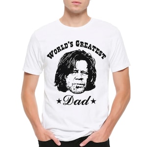 May include: A white short-sleeved t-shirt featuring a black graphic print of a man with long hair and a cigarette in his mouth. The text "WORLD'S GREATEST" is printed in a bold font above the face, and "Dad" is printed below with two stars.