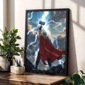 Peut inclure: Une impression d'art murale encadrée représentant une silhouette aux longs cheveux blonds portant une cape rouge, debout sur un terrain rocheux tout en tenant un marteau levé vers un ciel rempli d'éclairs bleu vif et de nuages d'orage sombres.