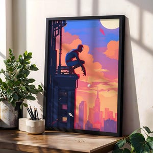 Puede incluir: Una lámina de arte vertical enmarcada que presenta una ilustración estilizada de un superhéroe con traje rojo y azul agachado en el borde de un edificio oscuro, con vistas al horizonte de una ciudad durante un atardecer vibrante con nubes naranjas, rosas y azules.