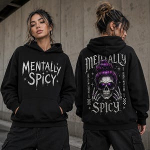 May include: A black hooded sweatshirt featuring the white text Mentally Spicy on the front. The back displays a graphic of a skull with purple hair in a bun, wearing sunglasses, with the text Mentally Spicy and Handle With Care.
