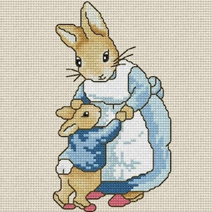 May include: A cross-stitch pattern on beige Aida cloth featuring two tan rabbits. The larger rabbit wears a light blue jacket and white apron, while the smaller rabbit wears a dark blue jacket. Both rabbits have pink accents on their feet.