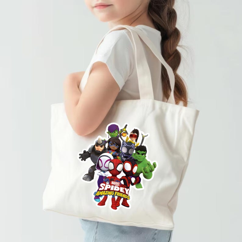 May include: A white canvas tote bag featuring a colorful graphic print of Marvel Spidey and His Amazing Friends characters, including Spider-Man, Ghost-Spider, Spin, Hulk, Black Panther, and Rhino, with the show title text printed in red and yellow.