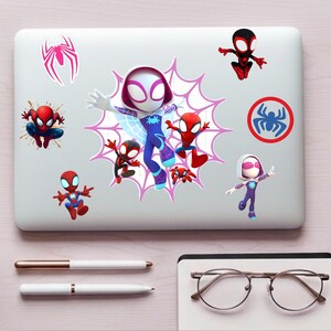 May include: A silver laptop lid decorated with multiple Spider-Man themed stickers. The collection includes a large central graphic of Ghost-Spider, several smaller Spider-Man character figures, a pink spider emblem, and a circular blue spider logo.