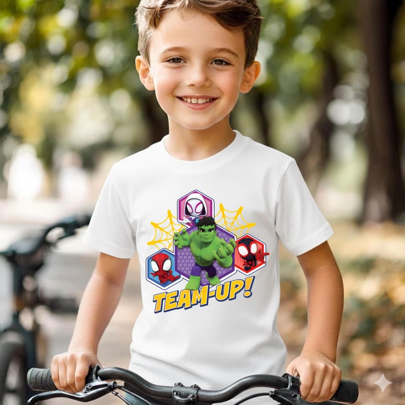 May include: A white short-sleeved t-shirt featuring a graphic print of the Hulk, Spider-Man, and Ghost-Spider inside hexagonal frames. The design includes yellow spiderwebs and the text "TEAM-UP!" in bold yellow letters with a blue outline.