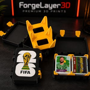 May include: A black and yellow plastic storage case for trading cards featuring the FIFA World Cup logo on the lid. The case is open, revealing a stack of soccer trading cards inside, and includes a separate yellow stand for displaying cards.