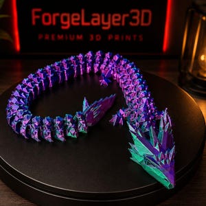 May include: A 3D-printed articulated dragon in shades of purple, blue, and green. The dragon is posed on a black surface, with the text "ForgeLayer3D PREMIUM 3D PRINTS" in the background.
