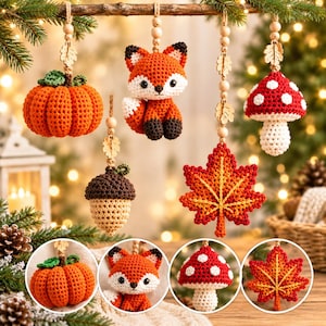 Op de afbeelding: Een collectie gehaakte herfstornamenten waaronder een oranje pompoen, een vos, een bruine eikel, een rood-witte paddenstoel en een rood-oranje esdoornblad, elk hangend aan een koord met houten kralen en kleine bladaccenten.