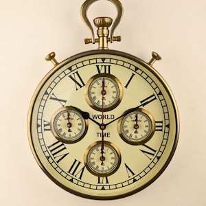 May include: A round wall clock with a brass-colored frame and a cream-colored face featuring black Roman numerals. The clock displays the text WORLD TIME and includes four smaller circular sub-dials, each with its own set of hands and markings.