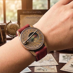May include: A vintage-style watch with a compass design. The watch has a bronze-colored face with a red canvas band. The face features a compass rose design with a red and green needle. The text "@AntiqueTouchGifts" and "AntiqueTouchGifts" are visible.