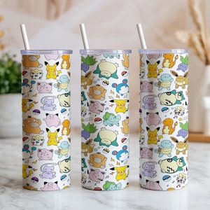 Peut inclure: Trois gobelets cylindriques hauts avec couvercles transparents et pailles blanches, arborant un motif répétitif de créatures de dessin animé colorées, incluant des personnages jaunes, roses, bleus et verts, ainsi que des icônes Poké Ball.