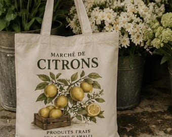 May include: Cream-colored tote bag with the words "Marché de Citrons" and a lemon illustration. The bag features a wooden crate filled with lemons and the text "Produits Frais de la Cote d'Amalfi Italie". The bag has two handles and is surrounded by flowers.