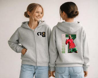 May include: A light gray zip-up hoodie featuring a graphic of a soccer player on the back. The front of the hoodie has the letters "CR7" with the number 7. The back has the player's image, name, and signature.
