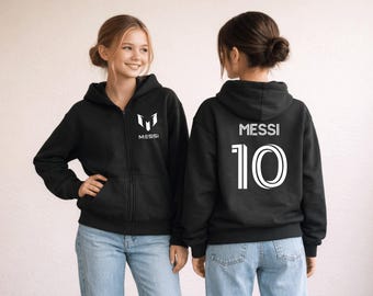 May include: Black zip-up hoodie with white "MESSI" and a logo on the front. The back of the hoodie displays "MESSI" and the number "10" in white. The hoodie is worn with blue jeans.