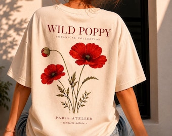 May include: Cream-colored t-shirt featuring a botanical illustration of red poppies with green stems and leaves. The text "WILD POPPY BOTANICAL COLLECTION" and "PARIS ATELIER - timeless nature -" are printed in red.