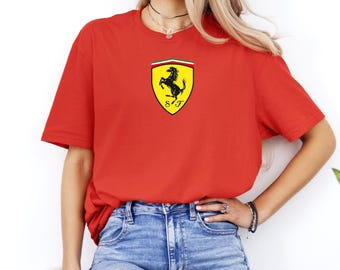 May include: A red t-shirt featuring the Ferrari logo. The logo is a black prancing horse on a yellow shield with green, white, and red stripes at the top. The shirt is a classic crew neck style.