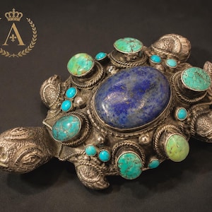 Può includere: Una statuetta di tartaruga in metallo color argento con una grande pietra ovale di lapislazzuli al centro del guscio. Il guscio è decorato con diverse pietre turchesi più piccole, rotonde e ovali, incastonate in bordi di metallo intrecciato.