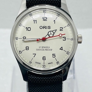 May include: An Oris wristwatch with a cream-coloured dial, black Arabic numerals, and a black textured strap. The dial features a Mercedes-style hour hand, a red second hand, and text reading ORIS, 17 JEWELS, SHOCK PROOF, and SWISS MADE.