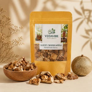 May include: A tan stand-up pouch labeled VEDAVIBE NATURALS KAVIT / WOOD APPLE Dried Fruit Pieces containing brown dried fruit chunks. A wooden bowl filled with the same fruit pieces sits beside a whole round wood apple and loose pieces.